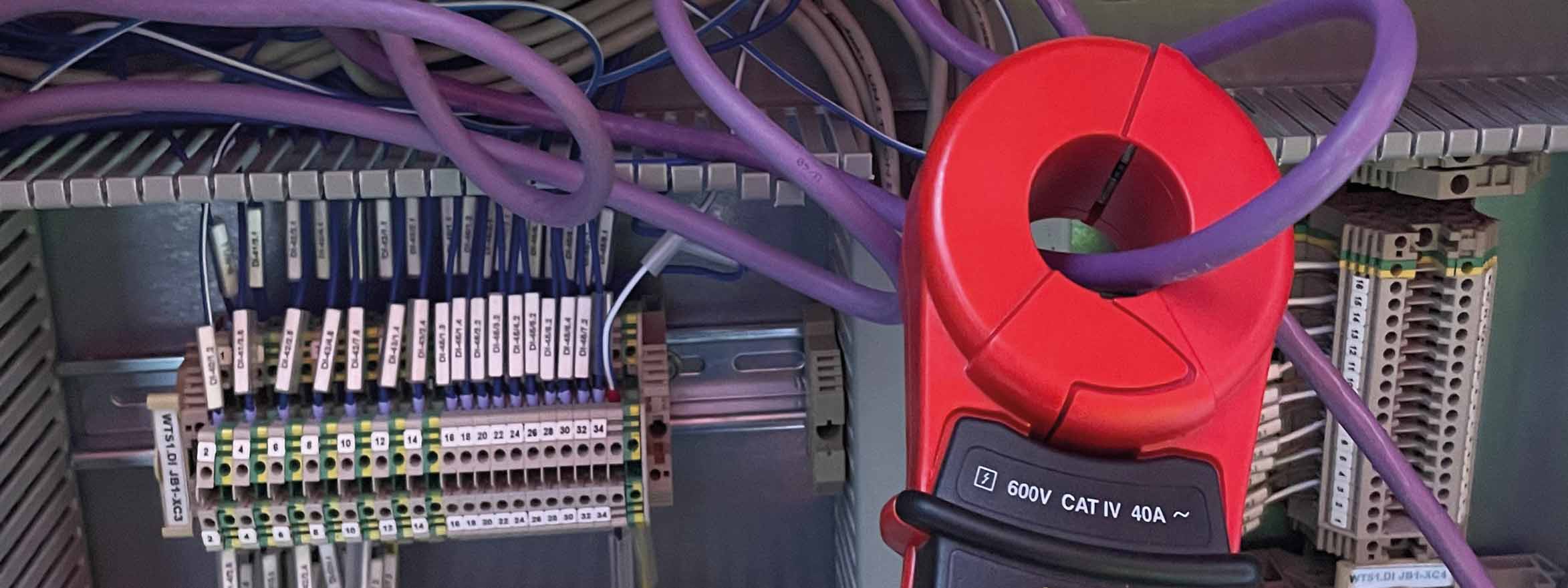 Clamp meter measuring current on a cable inside an industrial electrical cabinet.